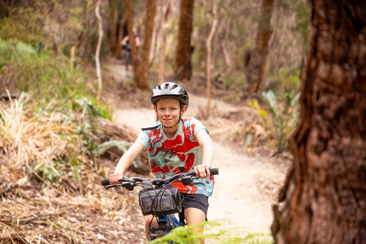 Child riding bike looking at the camera while on a trail in the forest. 