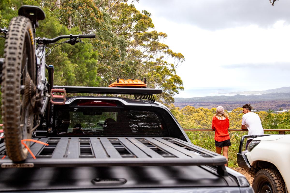 Two people looking at the view near parked vehicles with a bike and bike rack on the roof. 