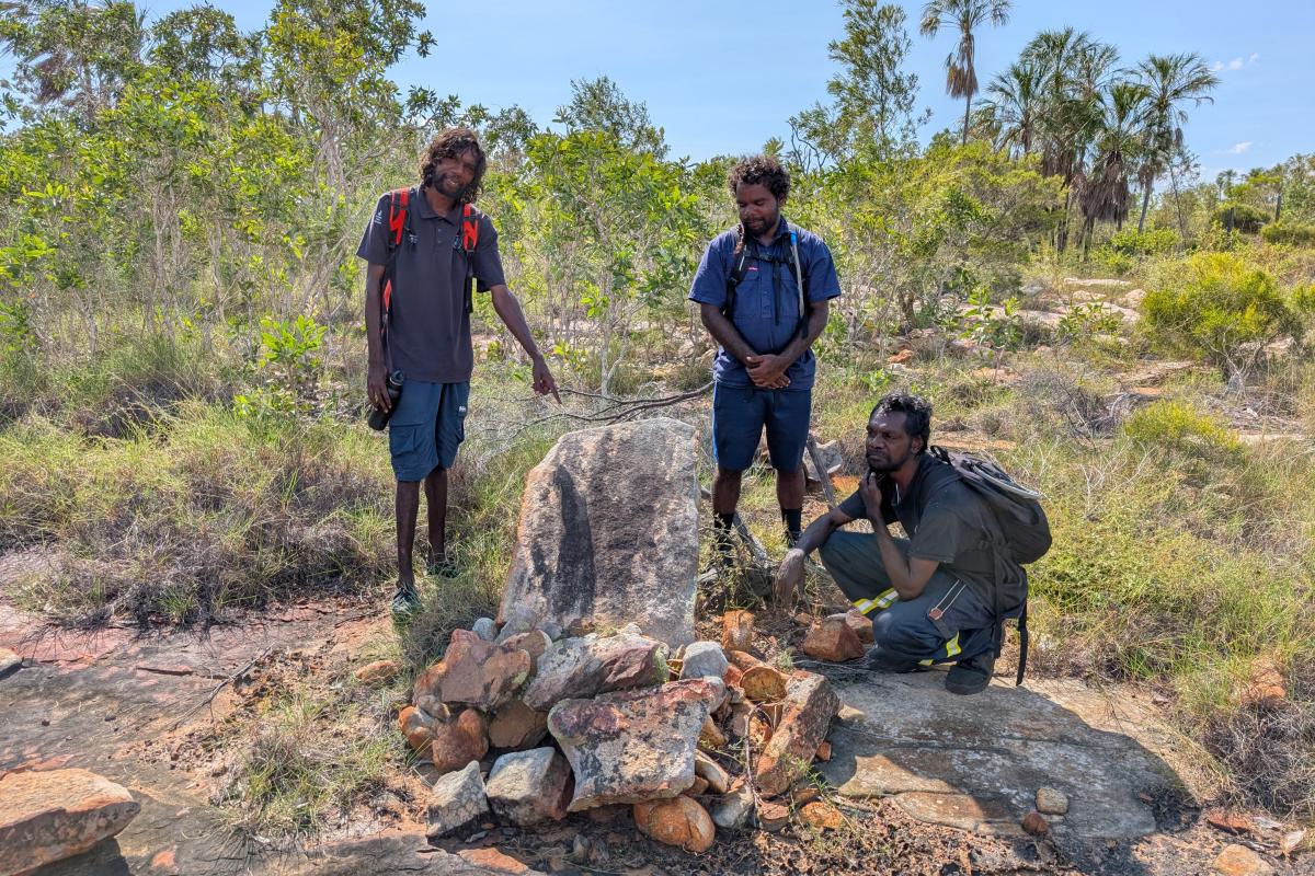 Three people standing near Aboriginal artefacts. 