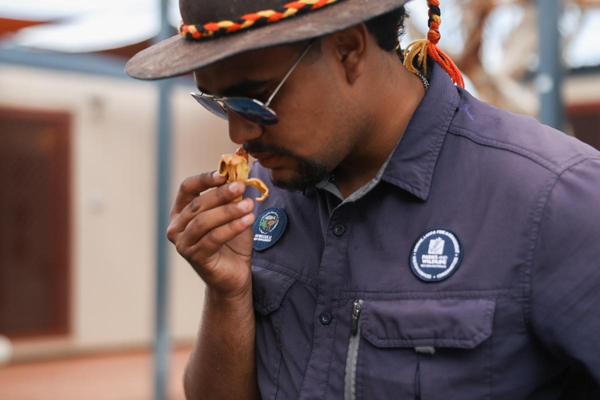 Person in blue uniform holding leaves near his face.