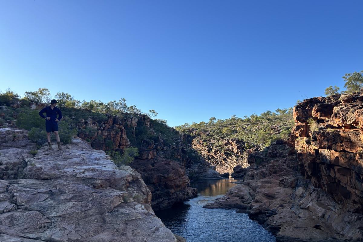 Person standing on the side of a rocky hill overlooking water. 