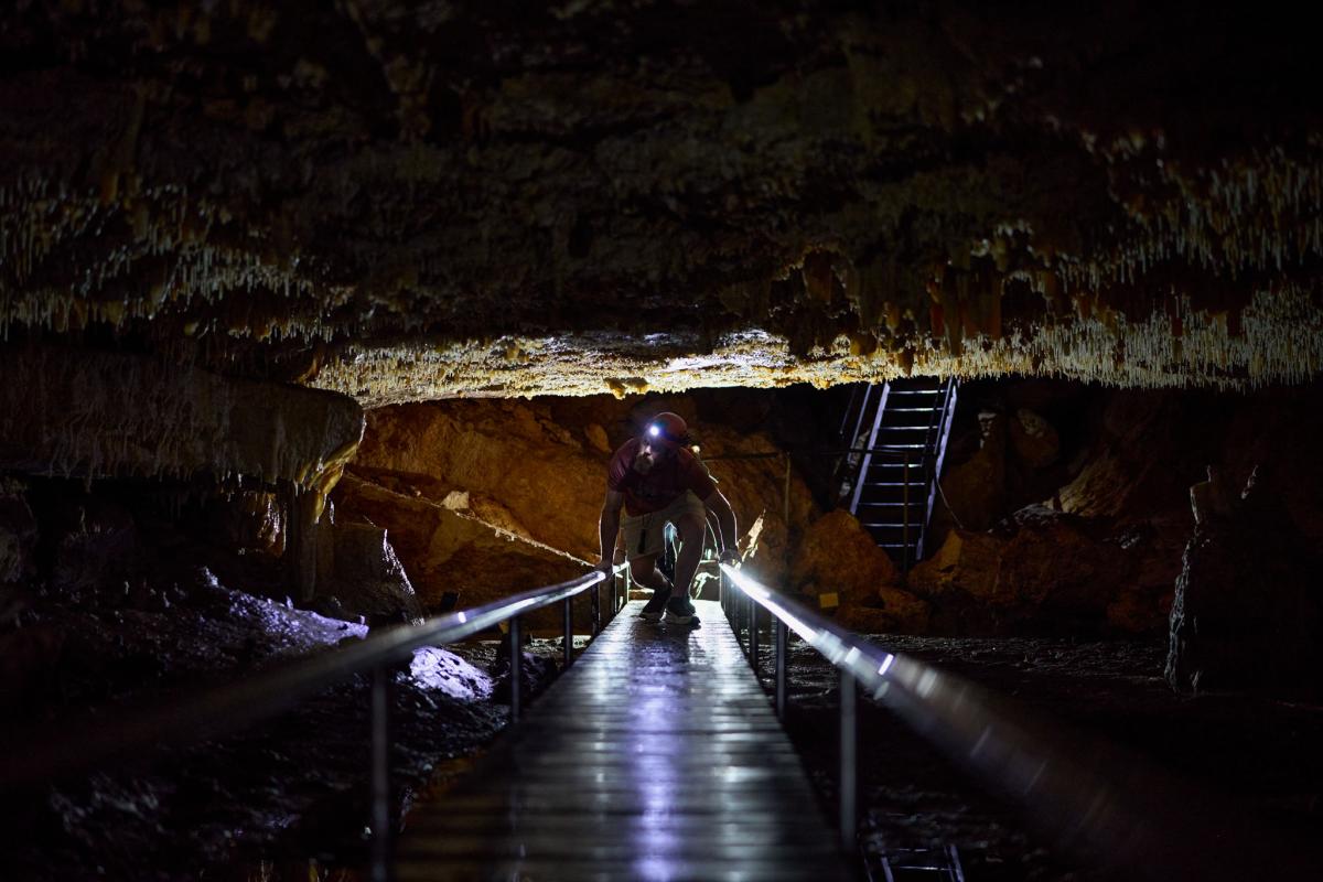 Man crouching and walking underneath cave roof along boardwalk. 
