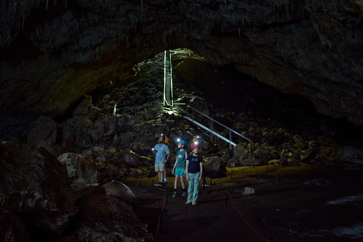 Family standing in first large chamber of Giants Cave, viewing cave formations by torchlight.