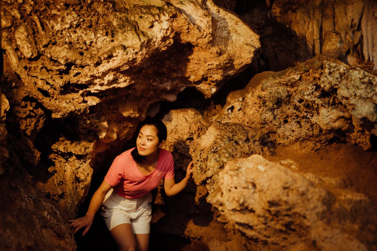 Lady crouching under limestone wall, navigating through cave.