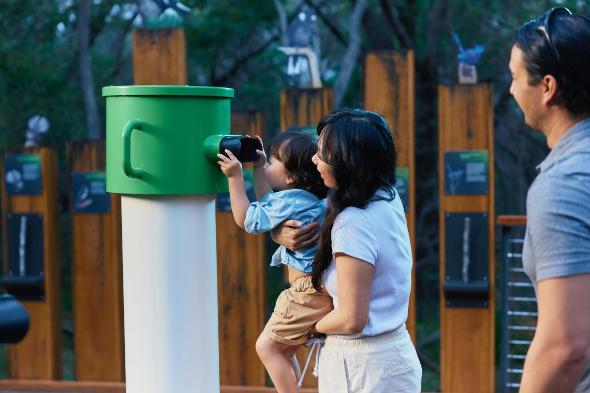 Lady holding child up to view eye piece of interactive augmented reality experience. 