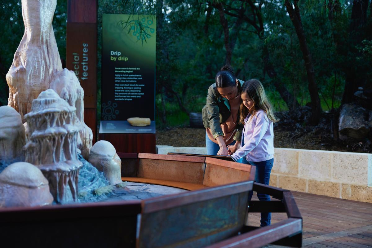 Mum and daughter reading a sign about cave formation, with a replica display of how those formations look inside the cave. 