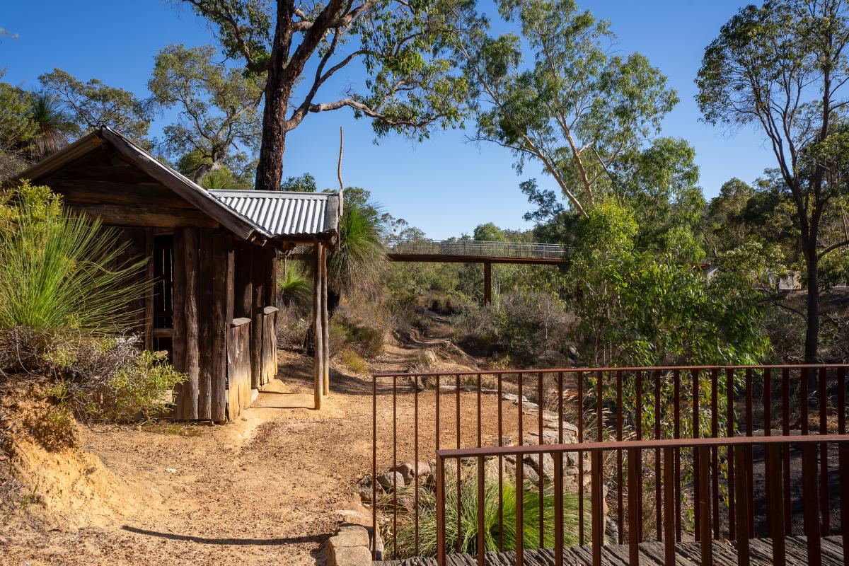 Small wood hut next to a trail with a view of a bridge in the distance. 