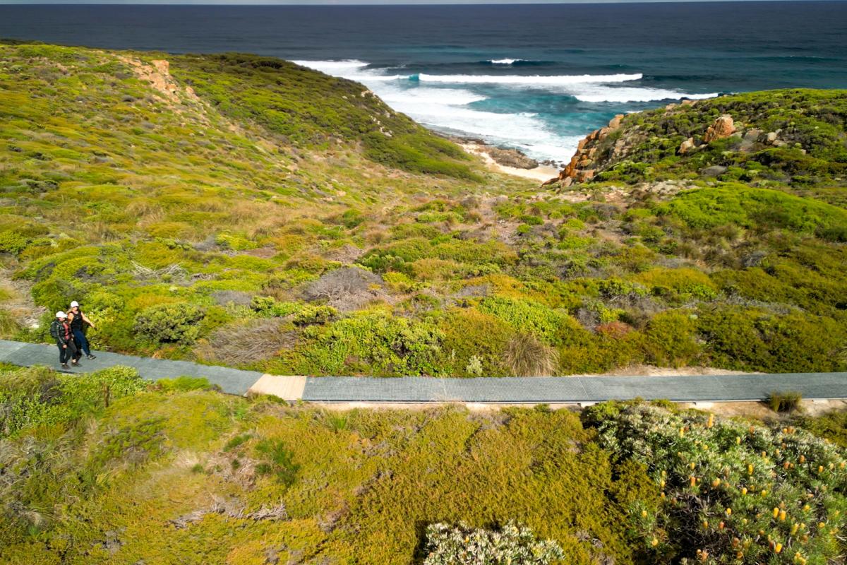 People walking on a man made path near the ocean. 