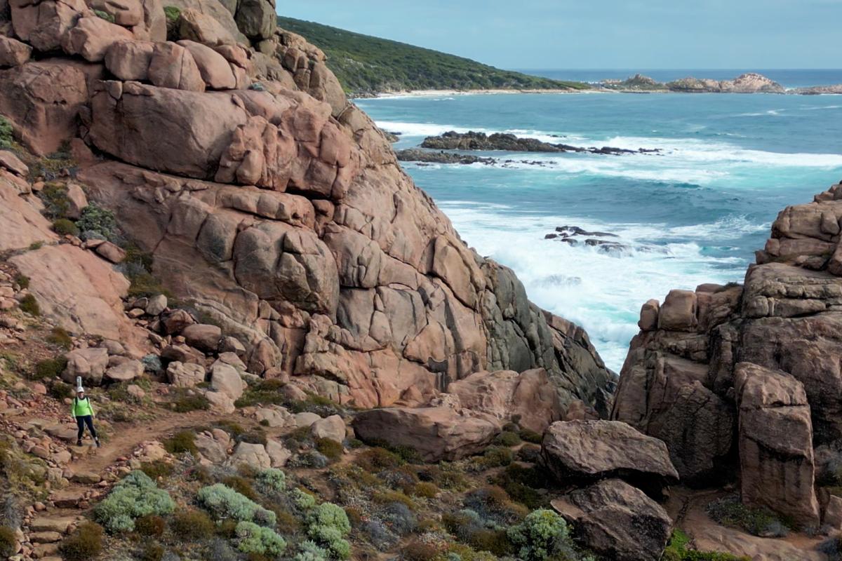 People hiking near large rocks near the ocean. 