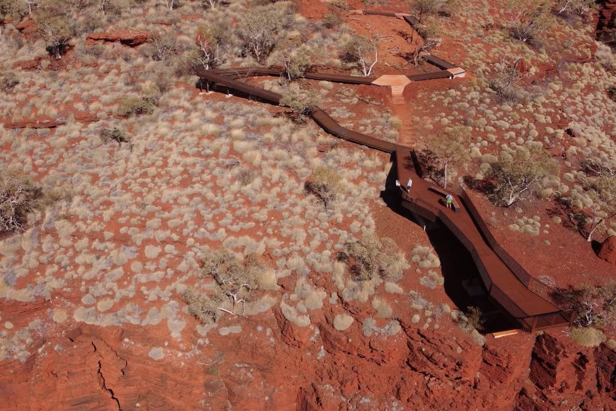 Aerial view of boardwalk surounded by red dirt and small shrubs. 