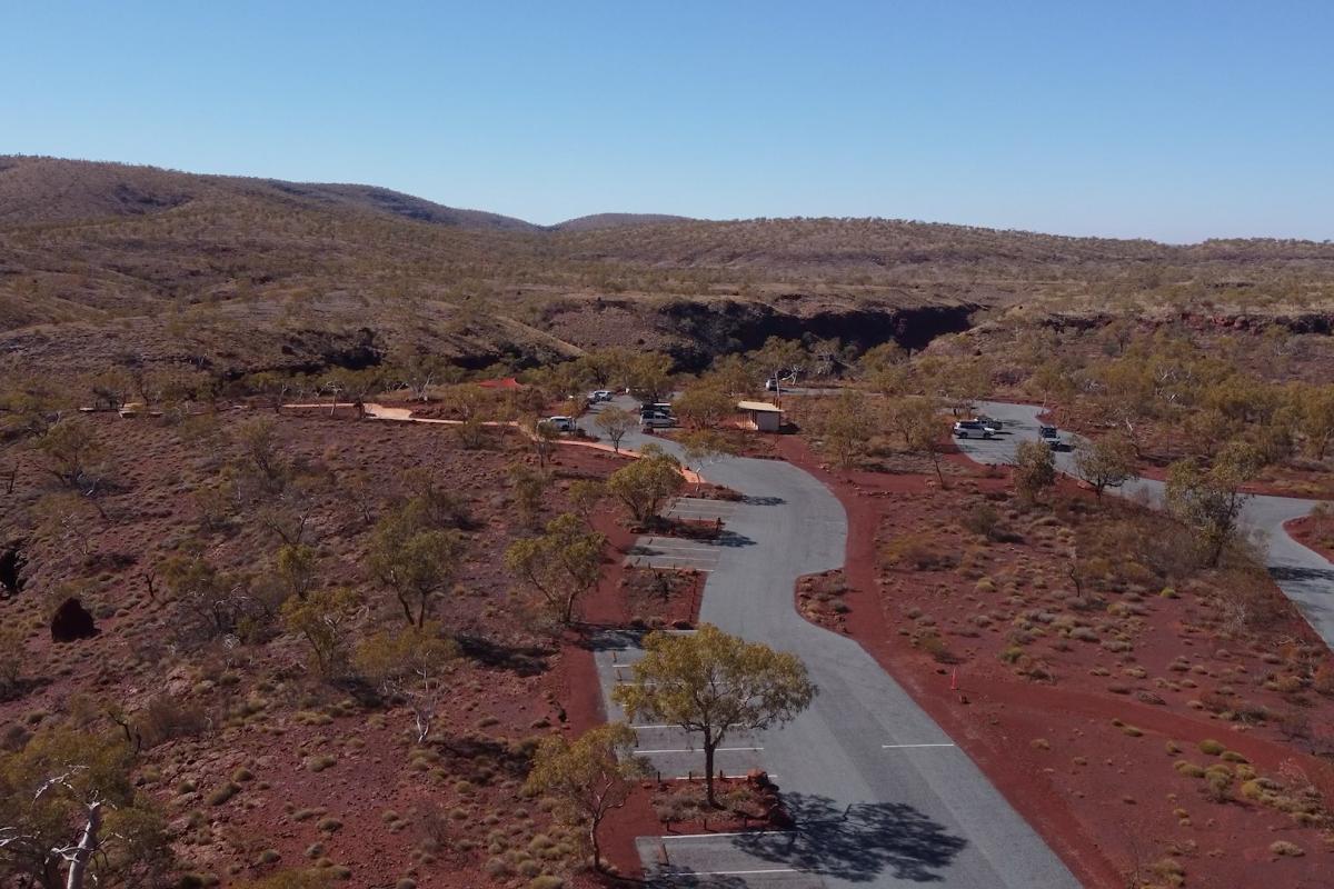 Aerial view of bitumen carpark that loops around. It is surrounded by red dirt and low shrubs. 