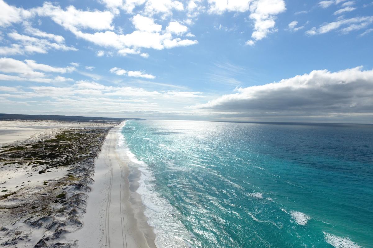 View of a stretch of white snady beach near the ocean.